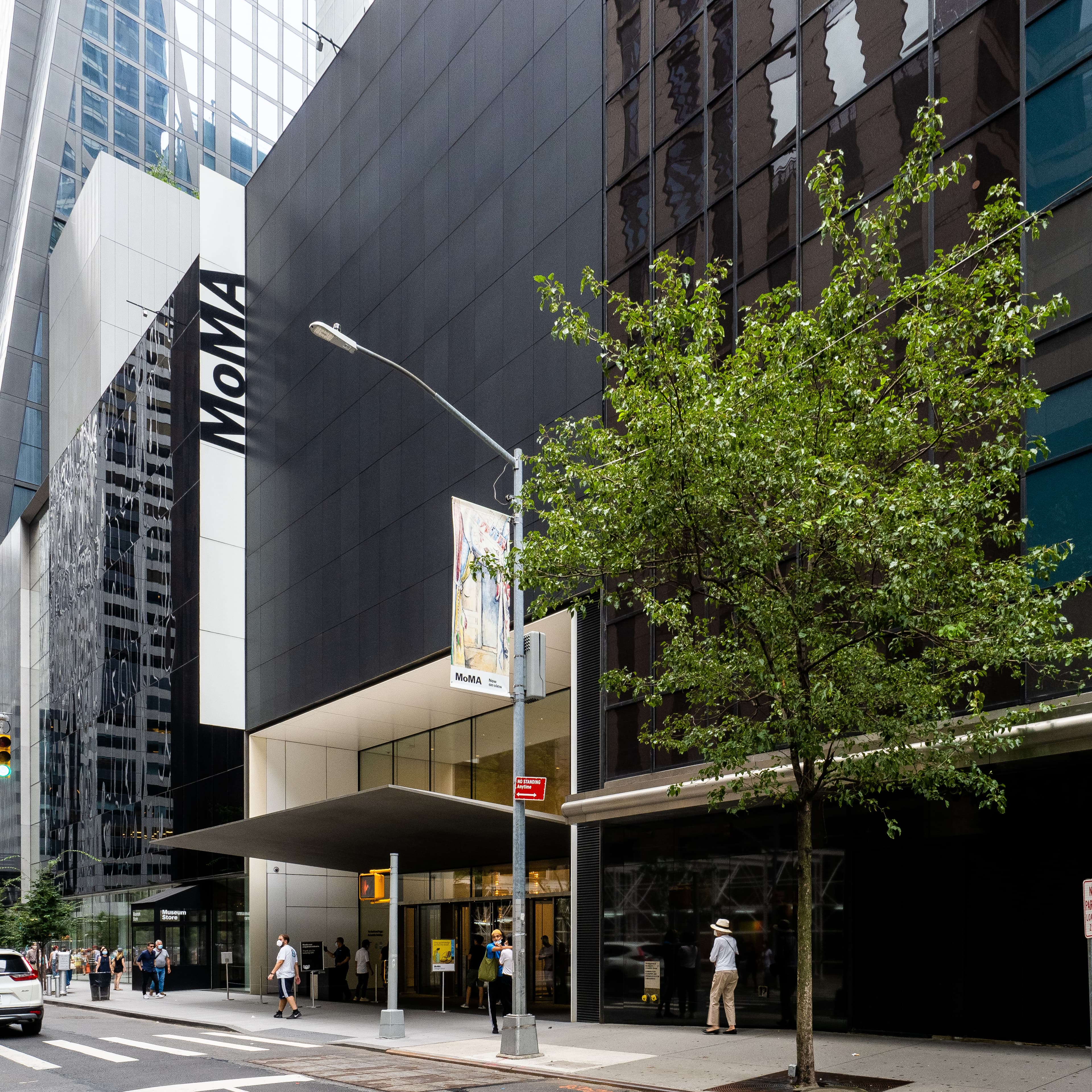 MoMA's glass facade and sculpture garden on West 53rd Street, with the museum's red banners, photographed August 21, 2021.