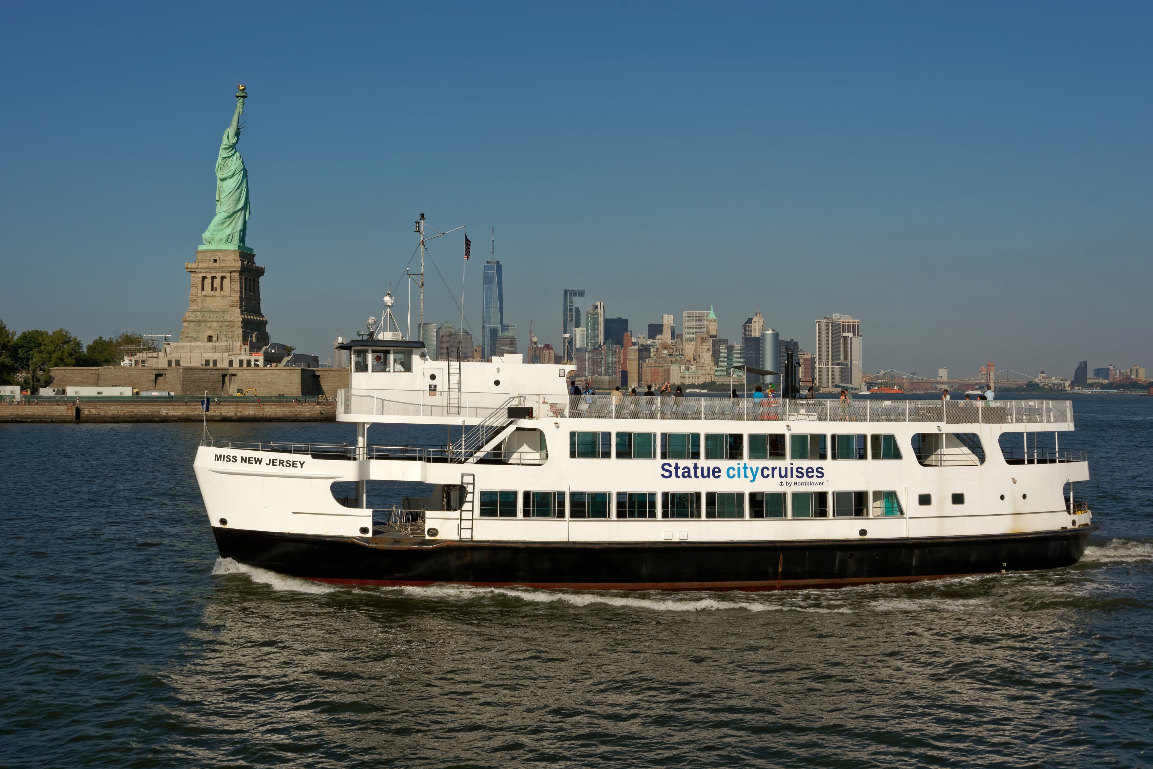 An authorized ferry crossing in front of Liberty Island, with the Statue of Liberty above the trees